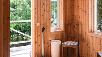 A wooden interior with a chair, a broom, and a window with a view of greenery.