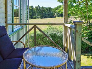 A wooden deck with a glass table and a chair, overlooking a grassy field and trees. - 5 Person Holiday Home in Kungshamn (Kungshamn)