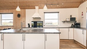 Una cocina moderna con techo de madera, armarios blancos, una isla grande e iluminación colgante.