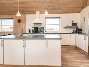 Eine moderne Küche mit Holzboden, weißen Schränken, einer großen Kochinsel und Pendelleuchten.