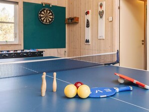 A ping pong table with balls, a paddle, and a table tennis net in a room with wooden walls and a dartboard.