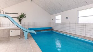 En indendørs swimmingpool med blå rutsjebane, flisebeklædte vægge og et loft med et gittermønster.