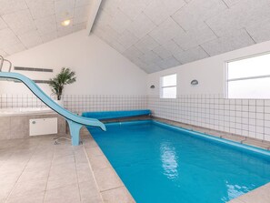 An indoor swimming pool with a blue slide, tiled walls, and a ceiling with a grid pattern. - 5 Star Holiday Home in Lokken (Lokken)
