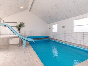 An indoor swimming pool with a blue slide, tiled walls, and a ceiling with recessed lighting.