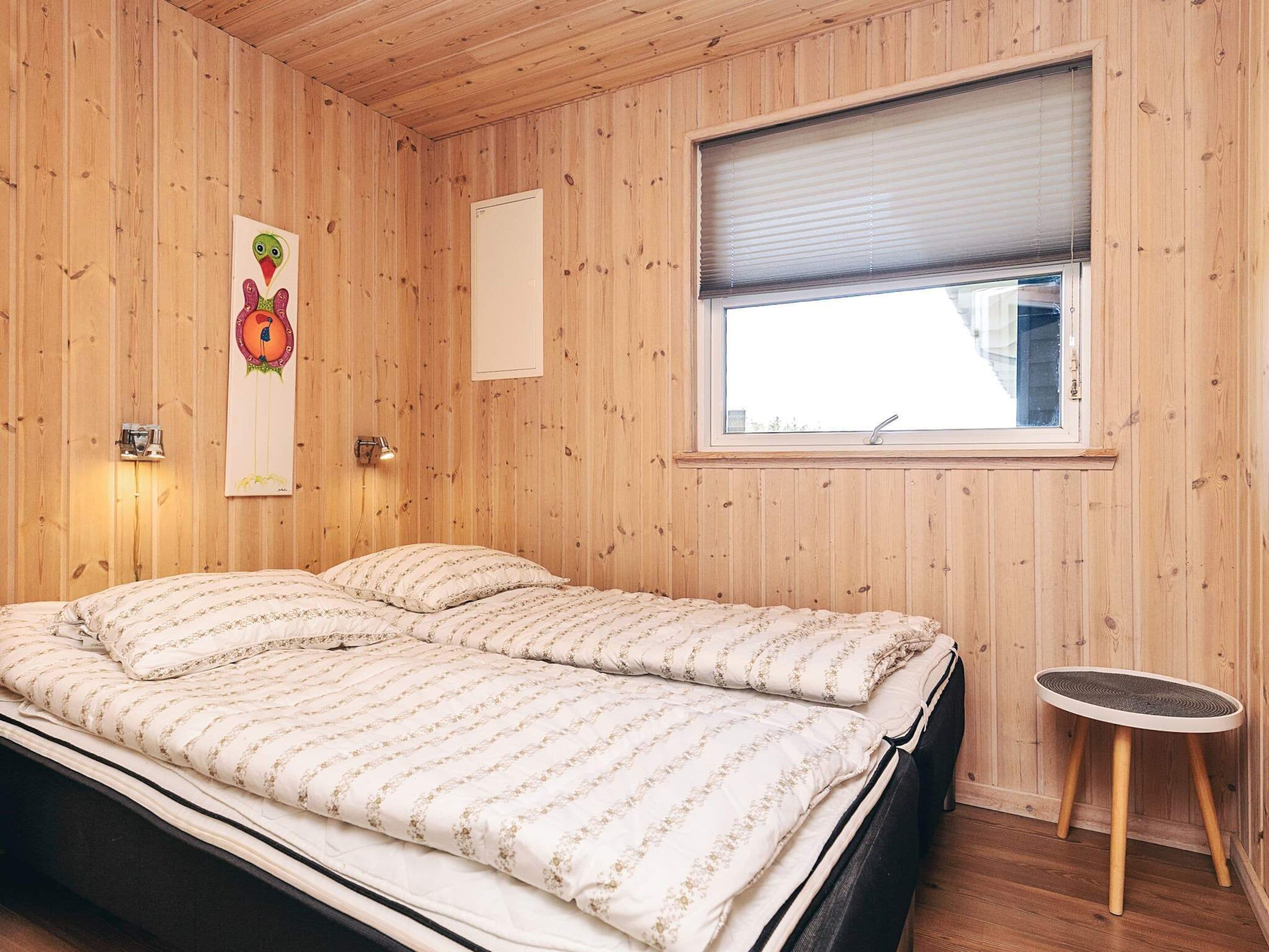 A room with wooden panel walls, a bed with floral bedding, a small round table, and a window with blinds.