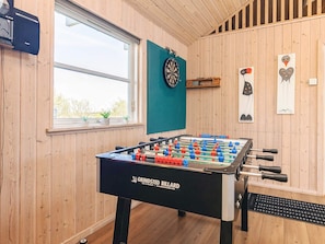 Ein Zimmer mit Holzwänden, einem Kicker, einer Dartscheibe und einem Fenster mit Pflanzen.