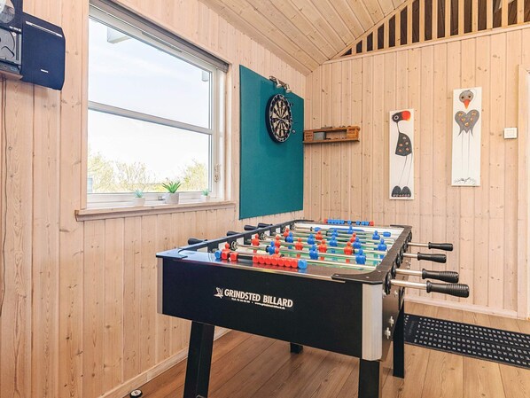 A room with wooden walls, a foosball table, a dartboard, and a window with plants. - 5 Star Holiday Home in Lokken (Lokken)