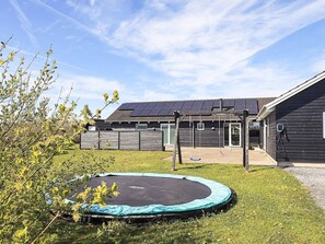 A residential property with a trampoline in the yard, a wooden fence, and a house with solar panels.