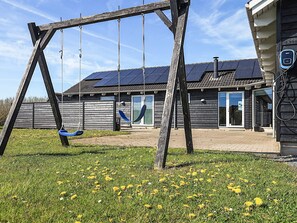 A wooden swing set in a grassy yard with a house featuring solar panels and a door.