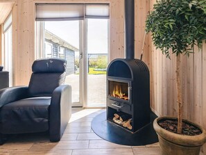 Una habitación moderna con un sillón de cuero negro, una estufa de leña y una planta en maceta.