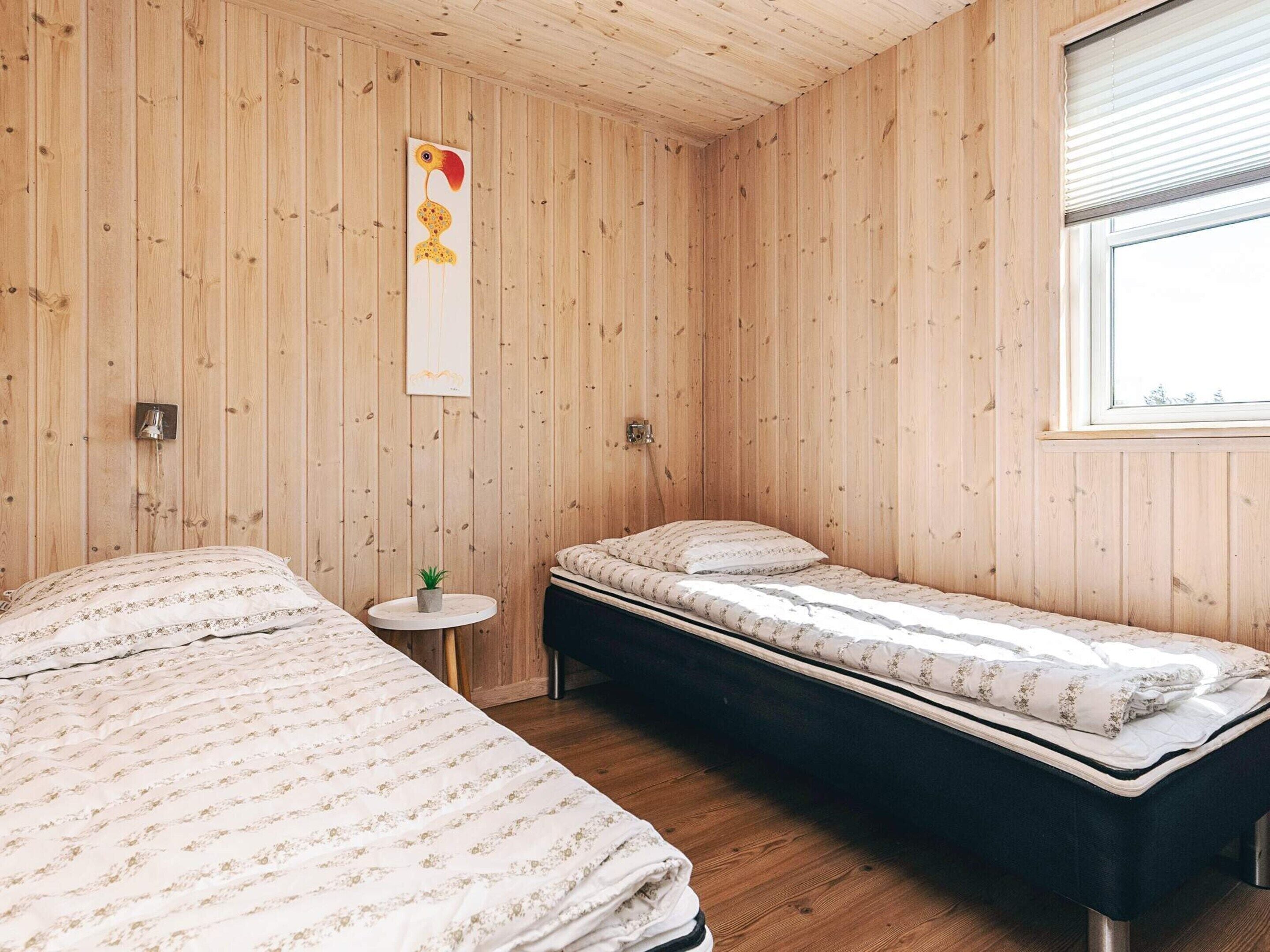 Une pièce aux murs en bois, avec deux lits dotés de draps à motifs floraux, une petite table ronde ornée d’une plante et un luminaire fixé au mur.