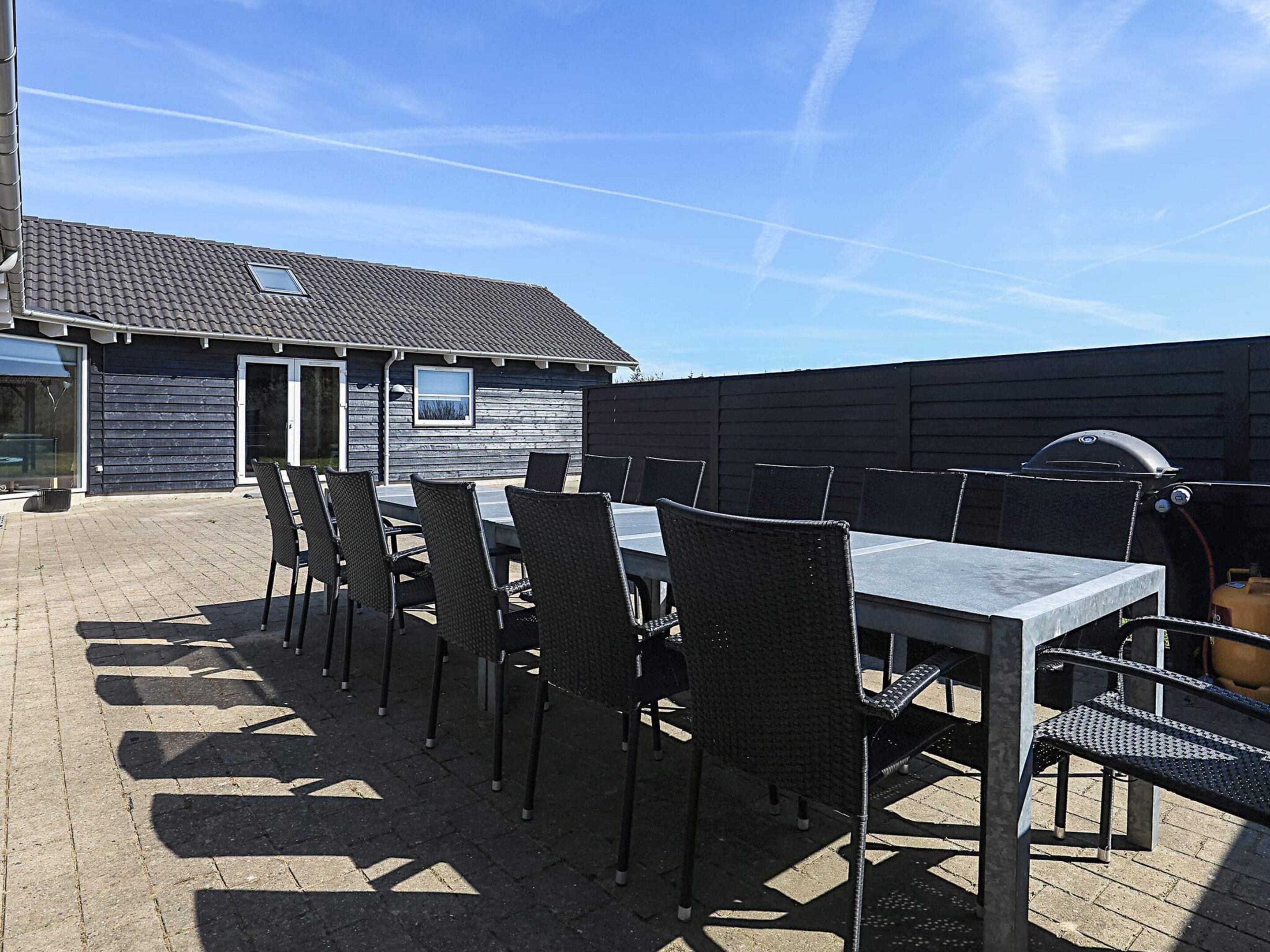 An outdoor patio with a table and chairs, a barbecue grill, and a building with a tiled roof.