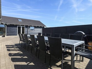 An outdoor patio with a table and chairs, a barbecue grill, and a building with a tiled roof. - 5 Star Holiday Home in Lokken (Lokken)