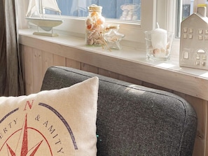 Ein Zimmer mit Fenster, ein Sessel mit Kissen und Dekoration auf der Fensterbank.