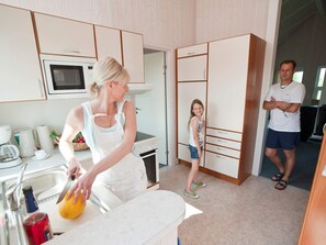 A kitchen with a microwave, a sink, and a stove. There is a person cutting fruit and another person standing by a wardrobe. - Holiday Home in Otterndorf (Otterndorf)