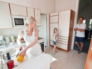 A kitchen with a microwave, a sink, and a stove. There is a person cutting fruit and another person standing by a wardrobe. - Holiday Home in Otterndorf (Otterndorf)