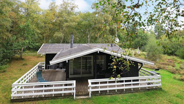 A cabin with a deck, a covered outdoor seating area, and a view of the surrounding forest.