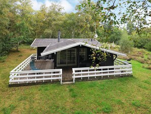 A cabin with a deck, a covered outdoor seating area, and a view of the surrounding forest.