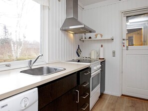 A kitchen with a dishwasher, stove, oven, and a window with a view of trees.