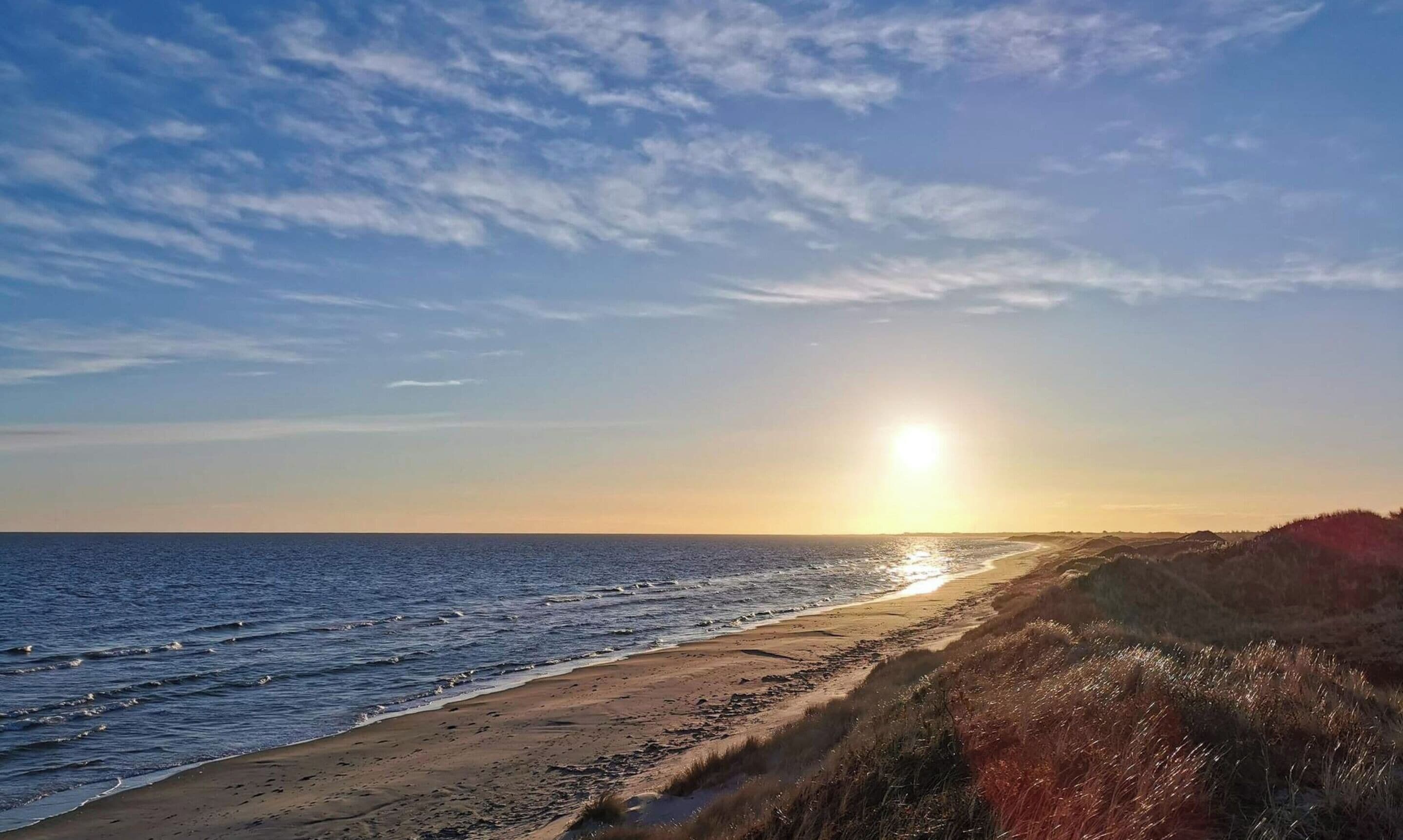 Een strand met een heldere lucht en de zon die onder- of boven de horizon verdwijnt.