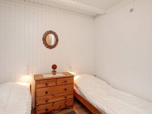 A bedroom with two single beds, a wooden dresser with a mirror, and a small potted plant.