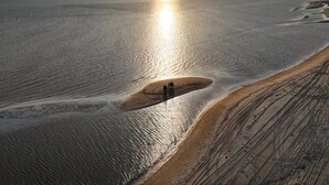 Un vaste paysage plat, avec une seule personne marchant le long d’un sentier étroit, au bord d’une étendue d’eau importante.