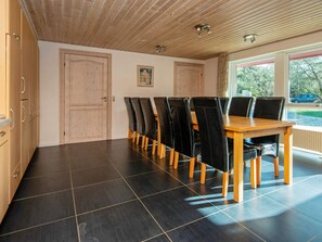 Un espace repas comprenant une table et des chaises en bois, un sol carrelé et une vue sur l’extérieur par une fenêtre.