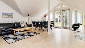 A spacious living room with a black leather sofa, a wooden coffee table, and a dining area with a table and chairs. - 6 Person Holiday Home in Jerup (Jerup)