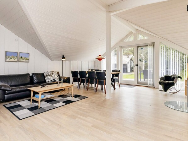 Un salon spacieux avec un canapé en cuir noir, une table basse en bois et un coin repas comprenant une table et des chaises.