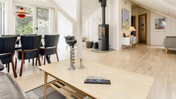 A spacious living area with a high ceiling, a modern fireplace, and a dining area with chairs and a table. - 6 Person Holiday Home in Jerup (Jerup)