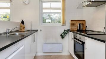A modern kitchen with white cabinets, a stainless steel sink, a window with curtains, and a built-in oven.