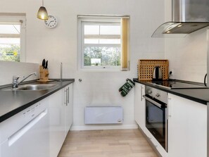 A modern kitchen with white cabinets, a stainless steel sink, a window with curtains, and a built-in oven.