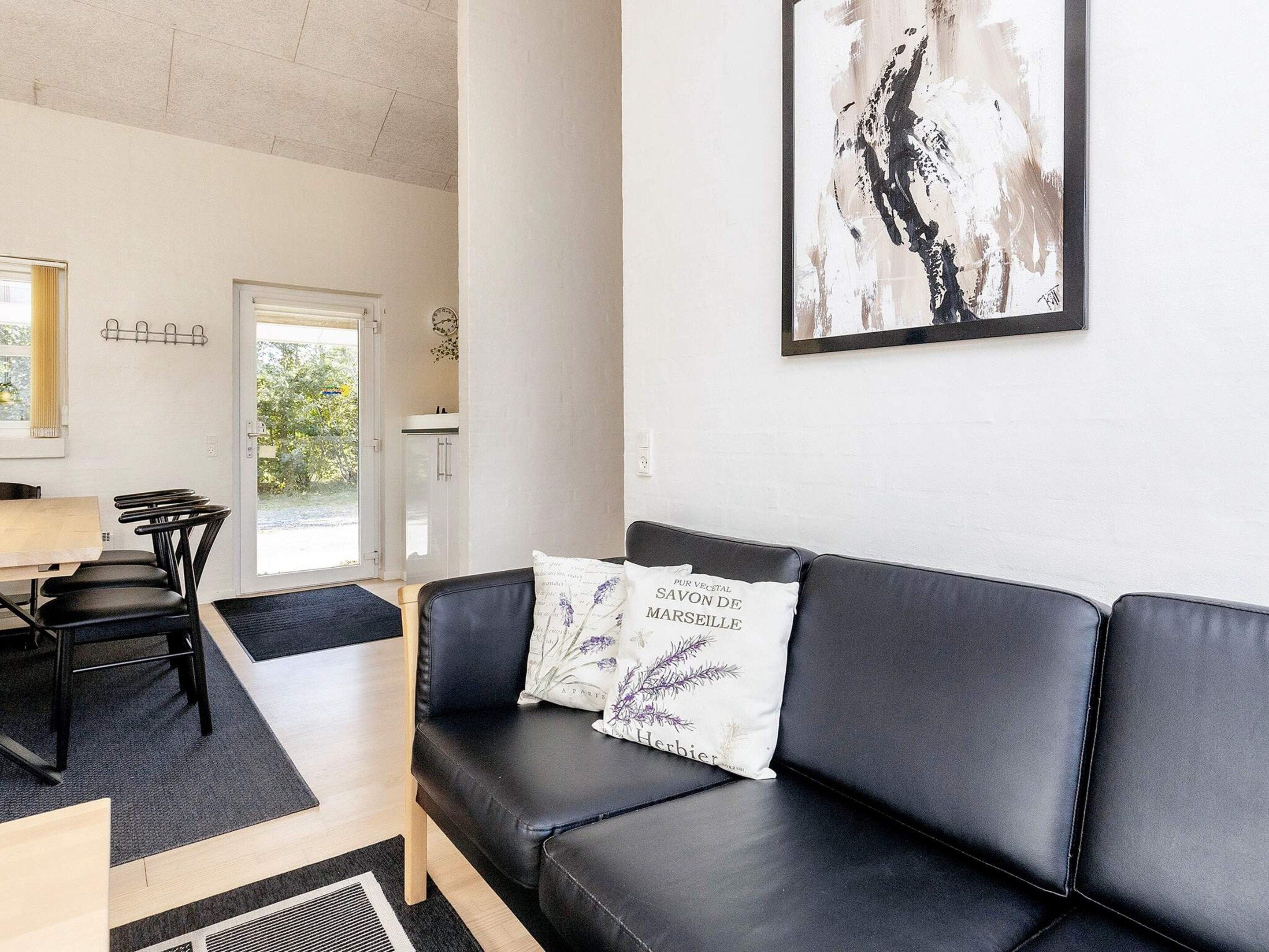 A modern living room with a black leather sofa, a dining table with chairs, and a kitchen area in the background.