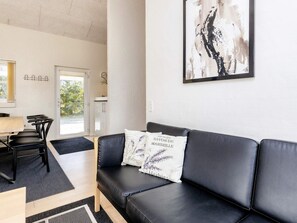 A modern living room with a black leather sofa, a dining table with chairs, and a kitchen area in the background. - 5 Star Holiday Home in Brovst (Brovst)