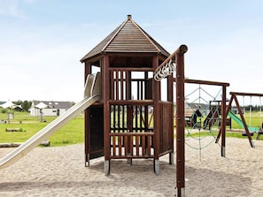 A wooden play structure with a slide and climbing net, set on a sandy playground. - 5 Star Holiday Home in Brovst (Brovst)