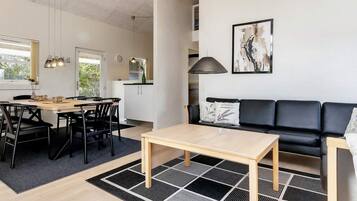 En moderne opholdsstue med spiseplads, sofa og et køkken i baggrunden.