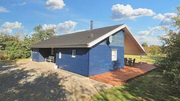 A blue single-story building with a sloped roof, a covered patio area, and a gravel driveway.