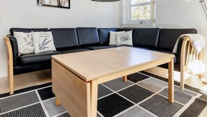 Uma sala de estar moderna com um sofá modular preto, uma mesa de centro de madeira e um tapete com padrão preto e branco.