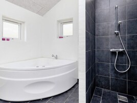 Un baño moderno con una bañera independiente, zona de ducha con cabezal de ducha manual y dos ventanas con cortinas rosadas.