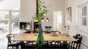 Uma área de refeições com mesa de madeira, cadeiras pretas e um vaso de vidro verde com uma planta.