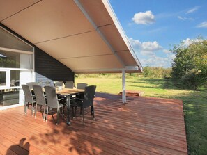 An outdoor patio with a table and chairs, a covered area, and a view of a grassy field.