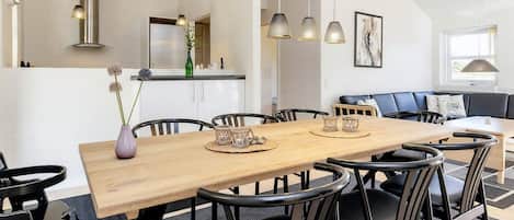 A modern dining area with a wooden table, black chairs, and pendant lighting.
