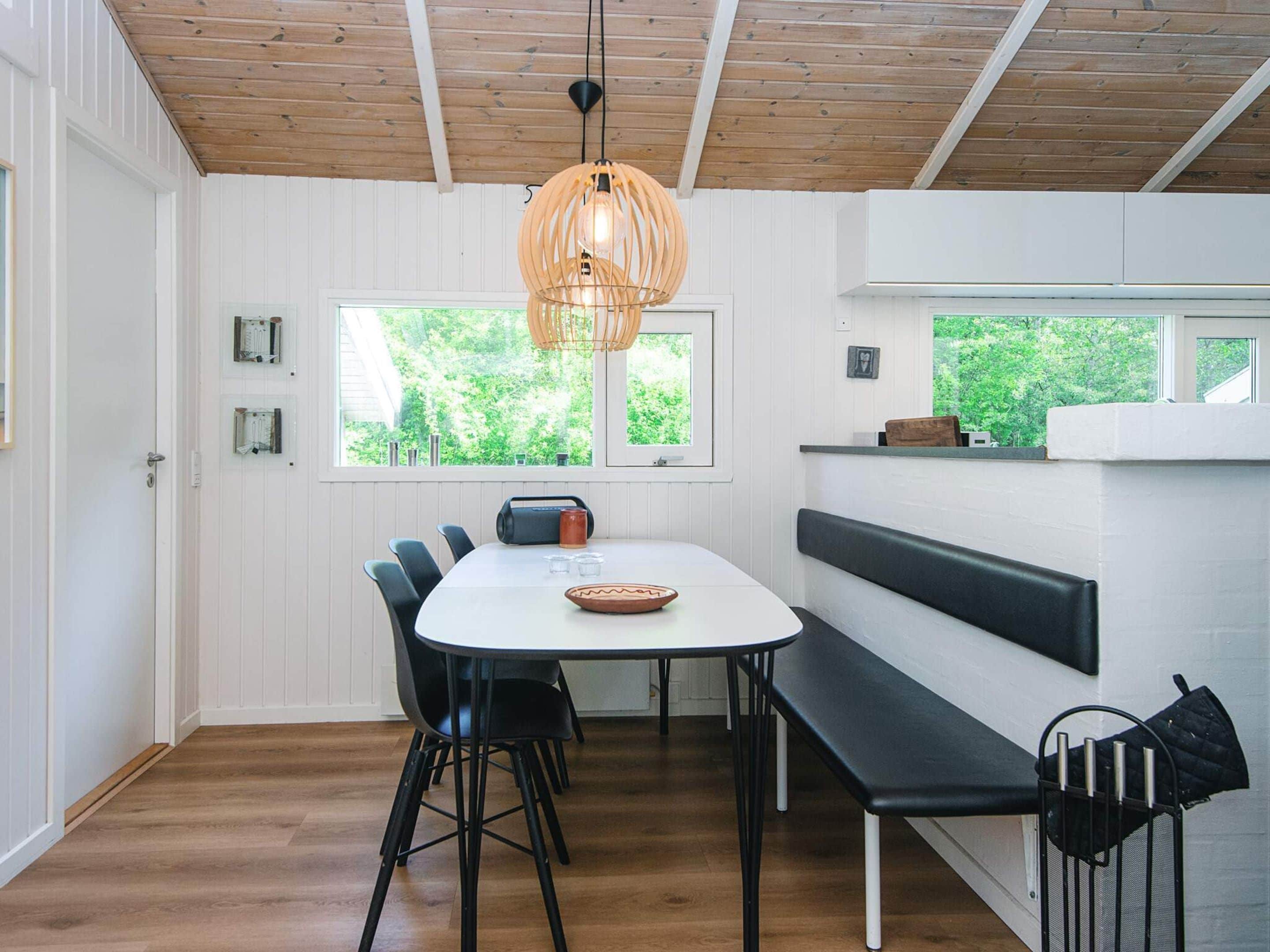 Un comedor moderno con una mesa blanca, sillas negras, techo de madera y una lámpara colgante.