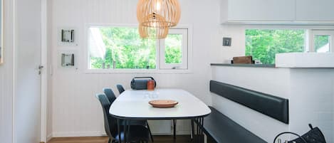 A modern dining area with a white table, black chairs, a wooden ceiling, and a hanging light fixture.