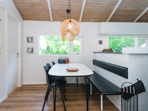 A modern dining area with a white table, black chairs, a wooden ceiling, and a hanging light fixture.