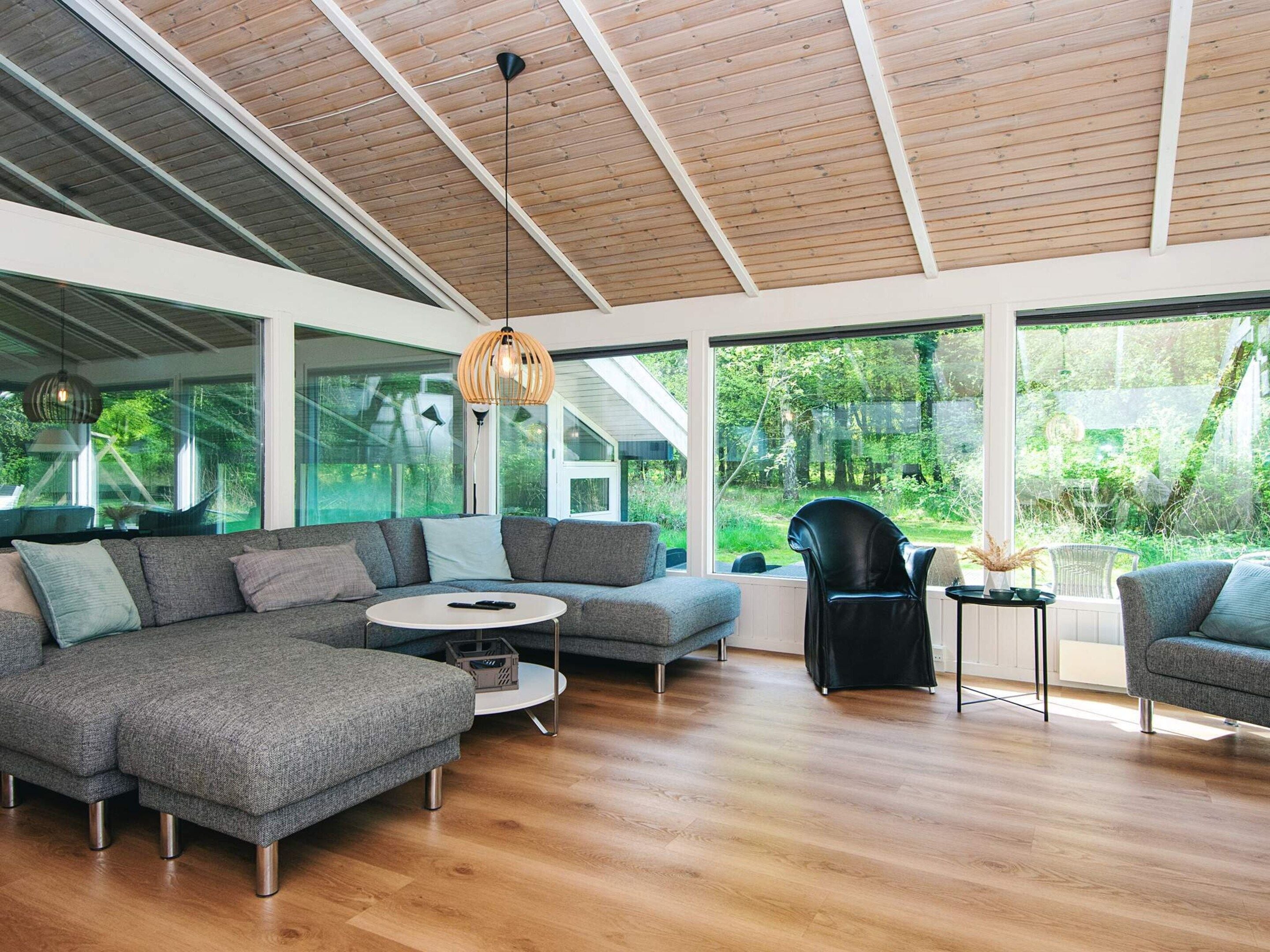 A modern living room with a sectional sofa, a round coffee table, and a black chair. Large windows offer a view of a lush garden.
