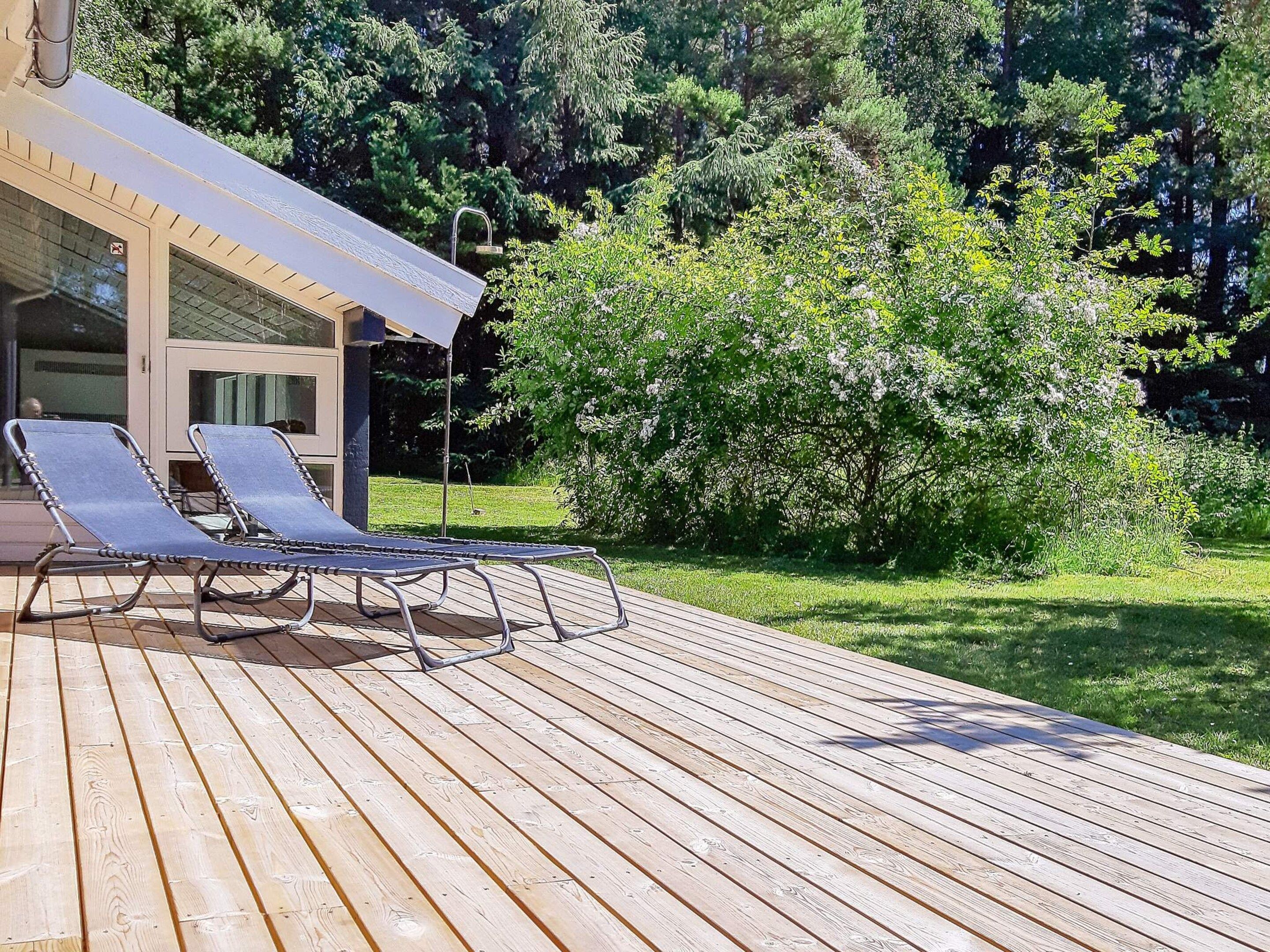 Terraza de madera con dos sillas reclinables y un porche cubierto con ventanal.