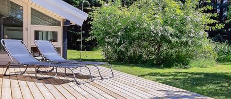 A wooden deck with two lounge chairs and a covered area with a window.