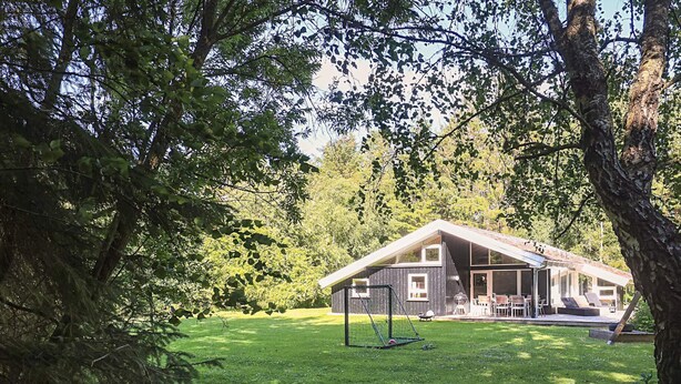 A modern house with a sloped roof, a patio with outdoor furniture, and a swing set in a lush green yard. - 4 Star Holiday Home in Bindslev (Bindslev)