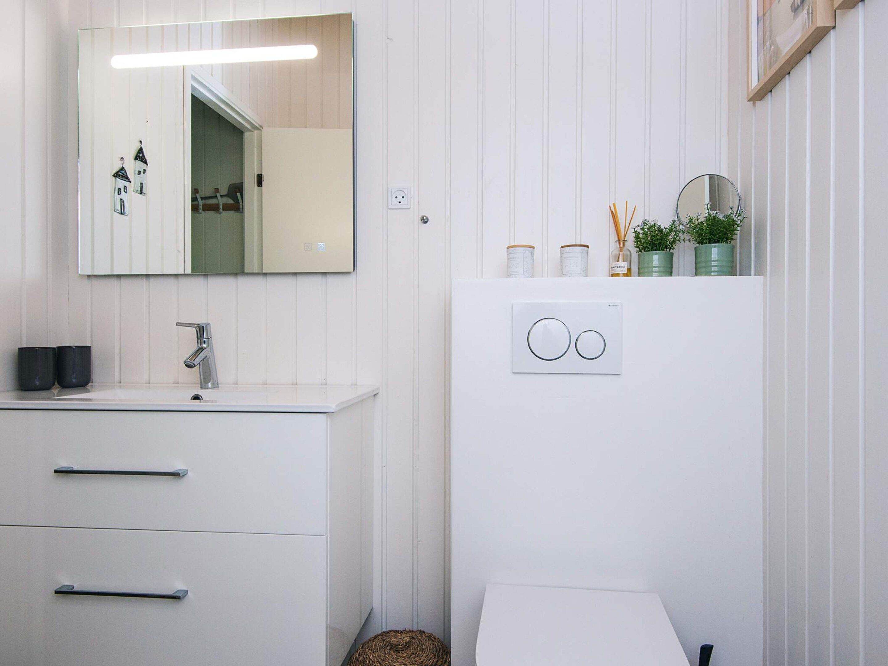 Une salle de bain moderne avec un meuble-lavabo blanc, un miroir, des toilettes et un luminaire fixé au mur.